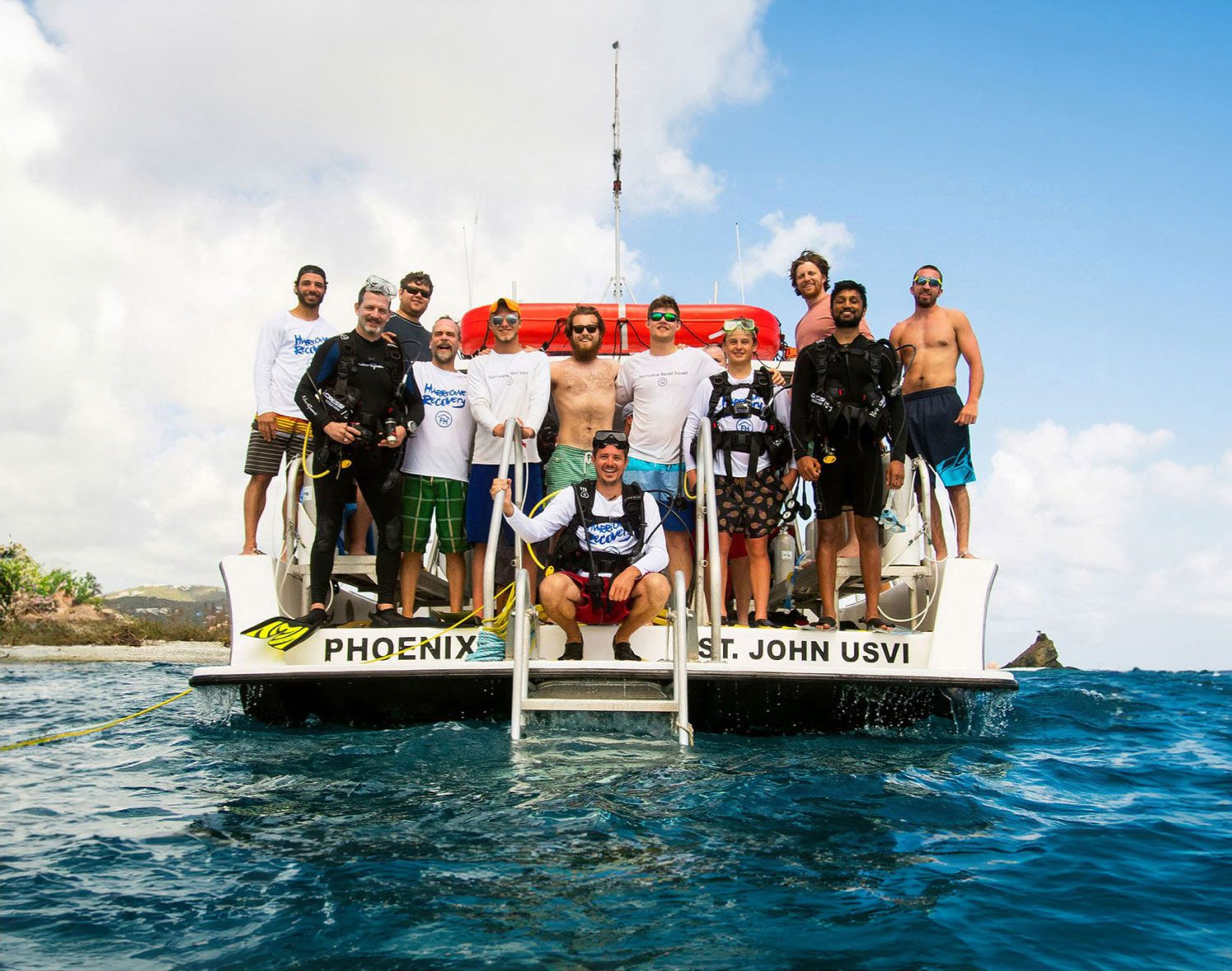 A group of young men in scuba gear gather on the stern of a boat in the Caribbean.