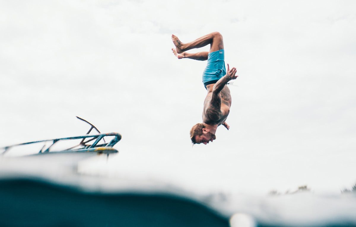 A young man celebrating his road to recovery flips upside down off a boat into the water.