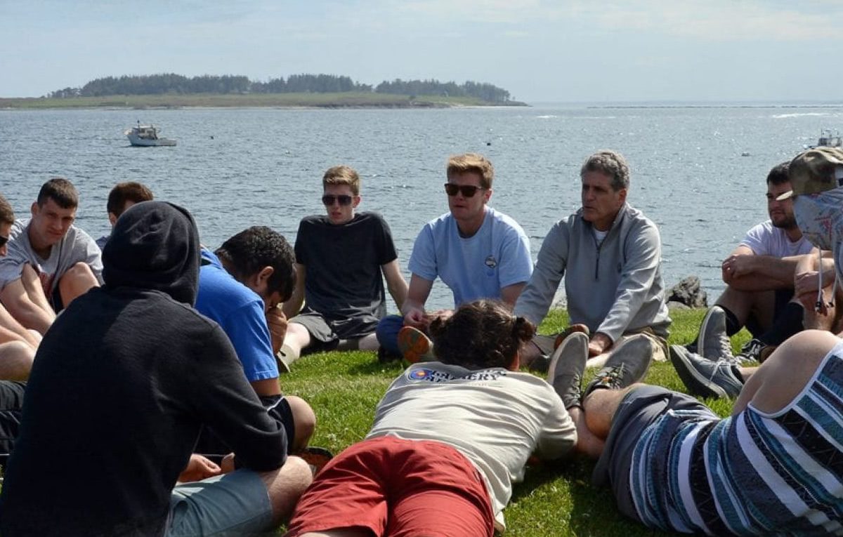 Young men and primary therapists gather and sit together talking by the ocean.