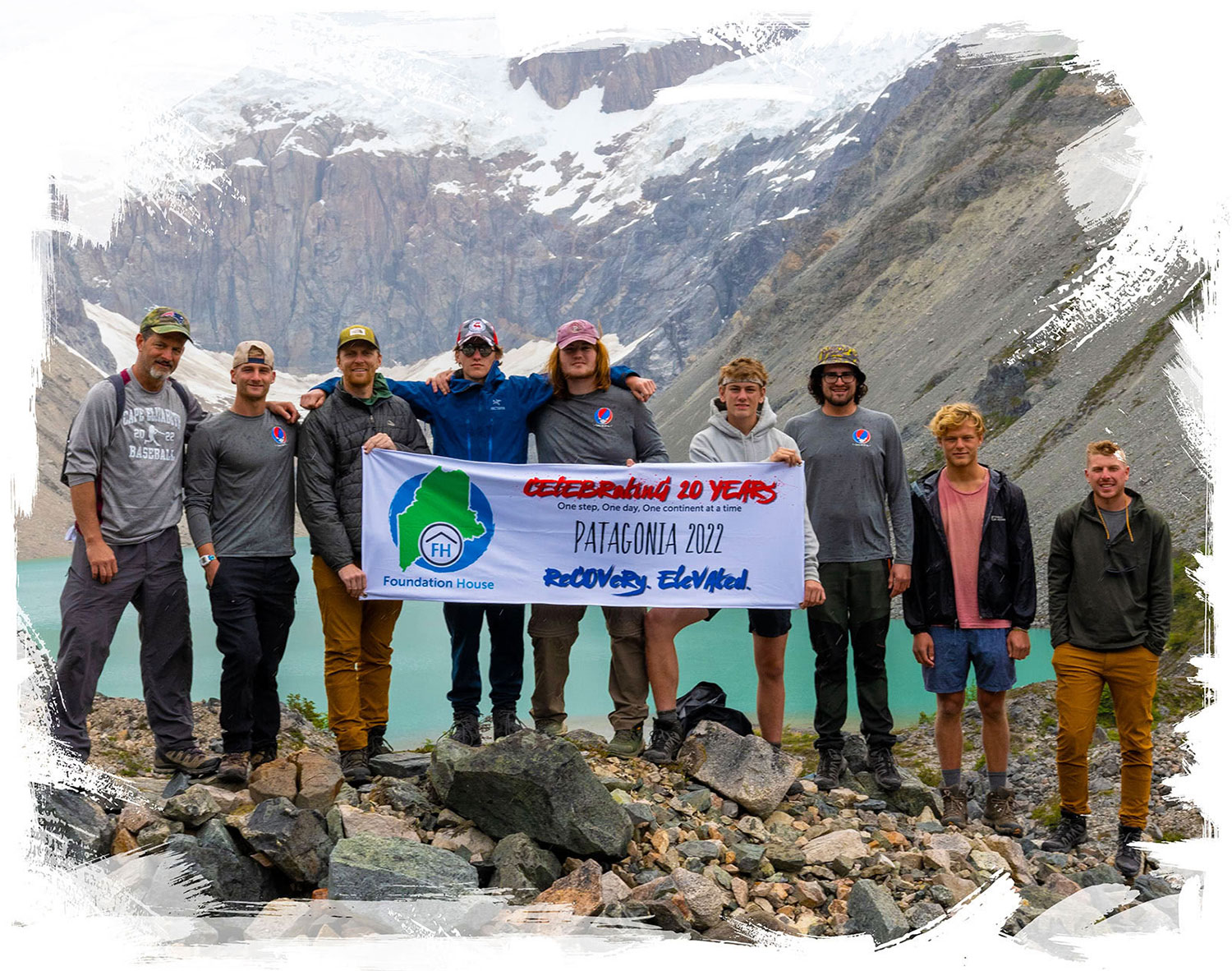 A group of men pose with a Recovery at Foundation House banner, under a mountain range in Patagonia, Chile.
