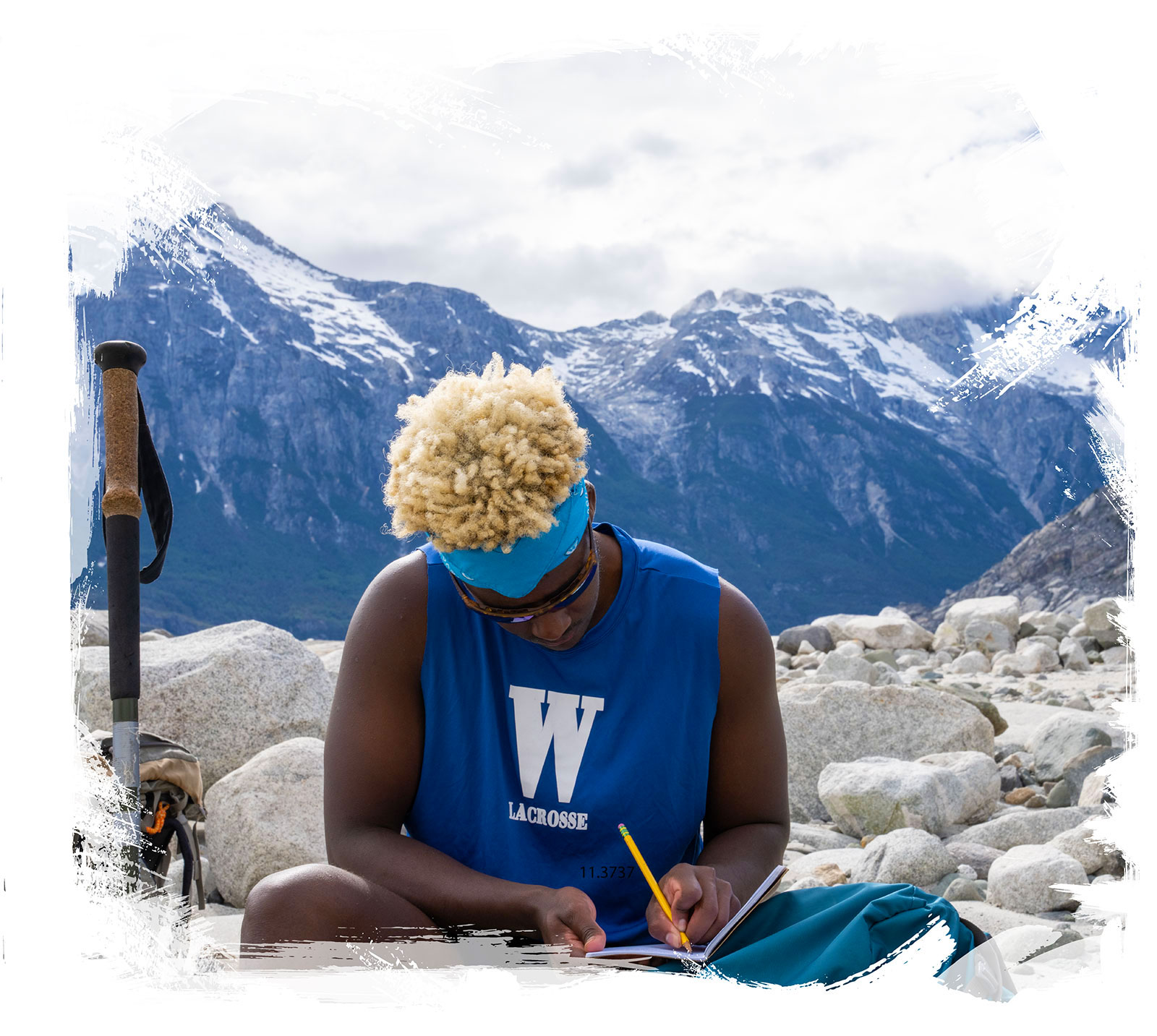 A young man sits to write in his journal on white rocks while hiking large snowy mountains in Patagonia chile.