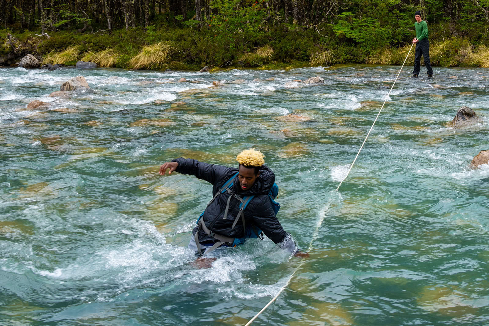 A young man crosses a rapid river in Patagonia, Chile.