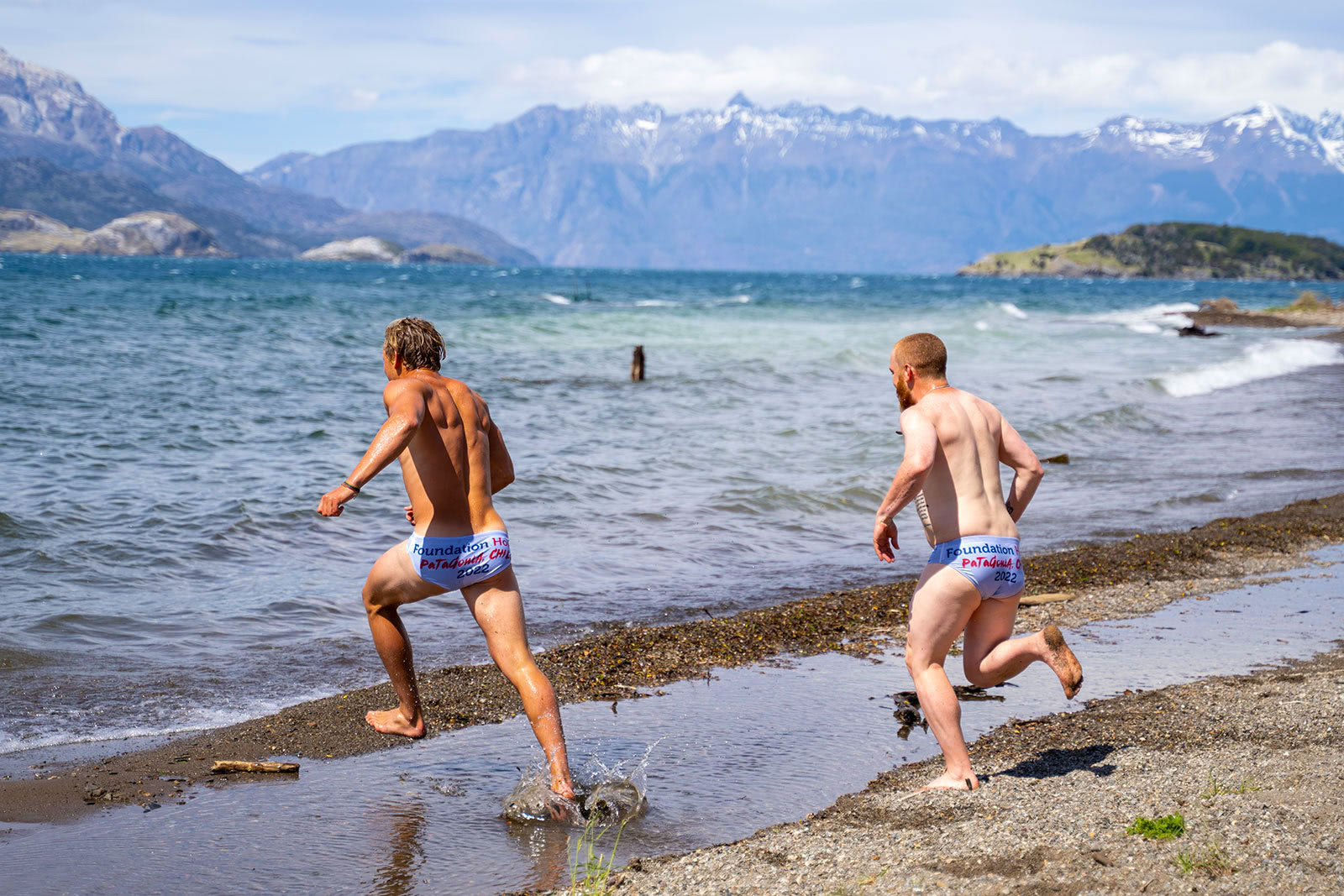 Two men in bathing suits run into icy cold ocean water in Patagonia, Chile